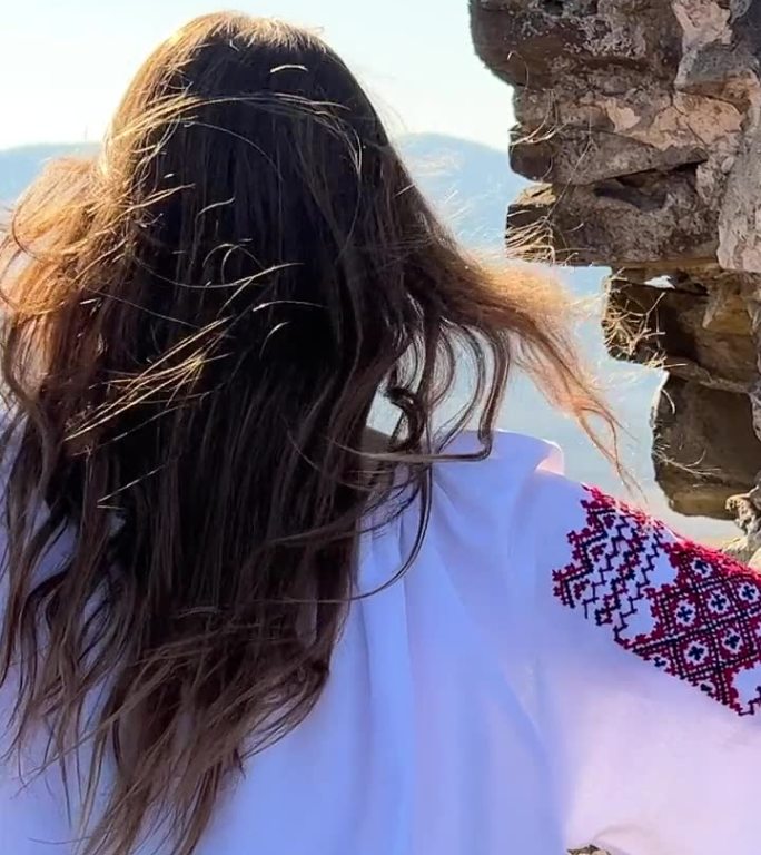 没有战争的乌克兰年轻女孩在一个古老的城堡废墟上，穿着刺绣衬衫，悲伤地看着周围的一切