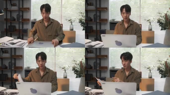 年轻英俊的韩国专业人士，在他舒适的家庭办公室里，沉浸在笔记本电脑的办公桌后面，用建筑的眼光制作现代设