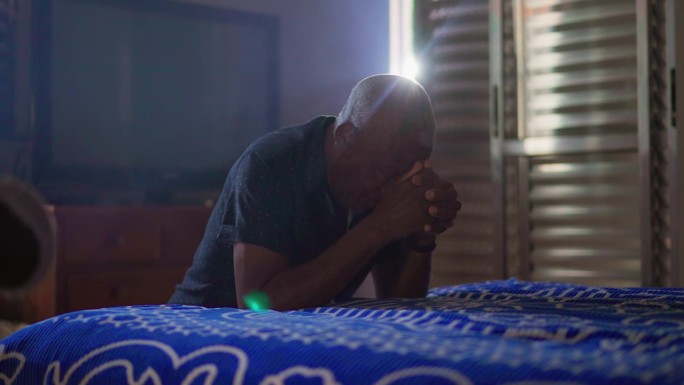 非裔美国老人在家床边祈祷。一个虔诚的黑人老人跪在地上祈祷。希望和信念的精神概念
