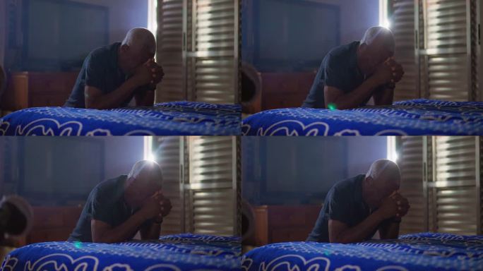 非裔美国老人在家床边祈祷。一个虔诚的黑人老人跪在地上祈祷。希望和信念的精神概念