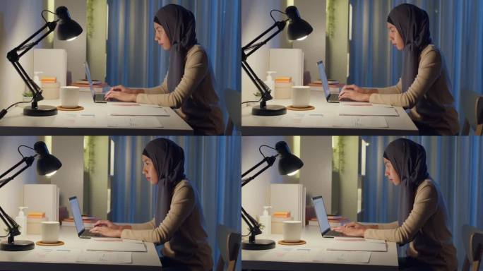 年轻快乐的亚洲穆斯林自由职业者妇女戴头巾休闲装打字键盘笔记本电脑在家里办公室加班，晚上工作。小企业主