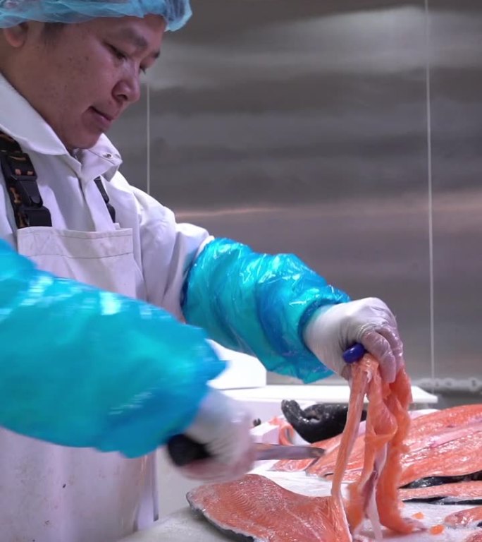 一名亚洲男子在鱼厂的餐桌上切三文鱼片。