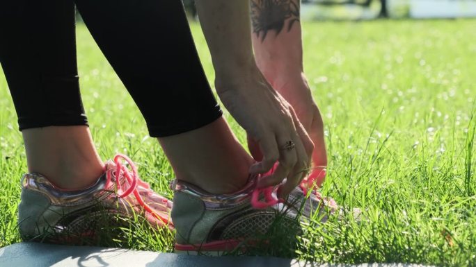 女性在公园里调整运动鞋的粉色鞋带