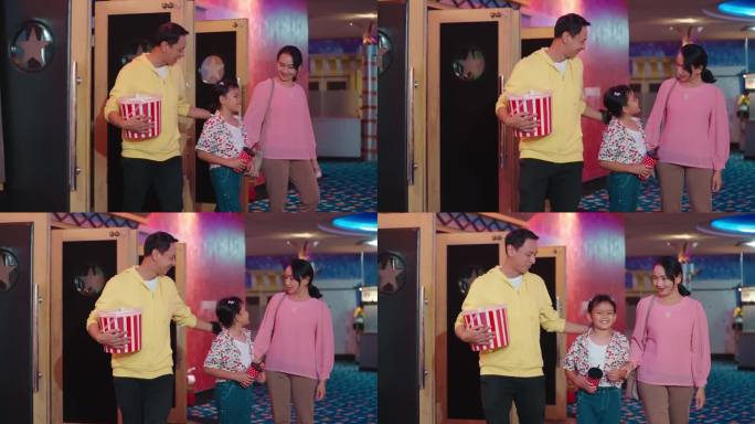 快乐的亚洲家庭在电影院门口吃着爆米花和饮料。一对父母带着女儿看完电影走出了电影院的出口。快乐亚洲家庭