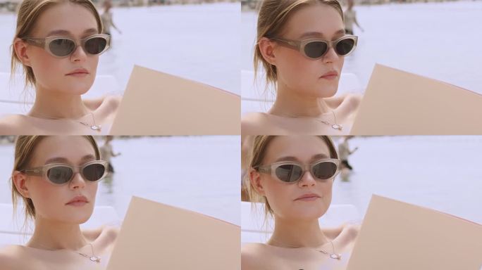 一个戴着墨镜的女孩在沙滩上的画像。一个年轻的美女躺在沙滩上或泳池边读杂志或书。在背景中，一个男孩和一