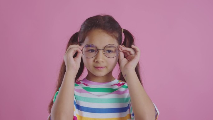 可爱的女孩戴着粉红色背景的眼镜。