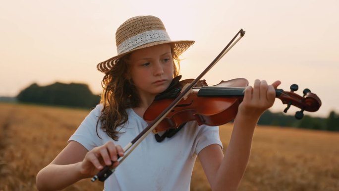 日落时分，戴着太阳帽的女孩拉着小提琴，在金色的麦田里演奏着迷人的旋律