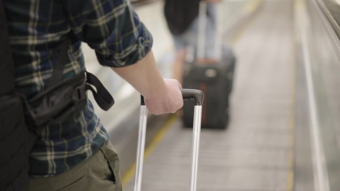 一名亚洲乘客带着带轮子的旅行袋走在移动走道上穿过机场航站楼