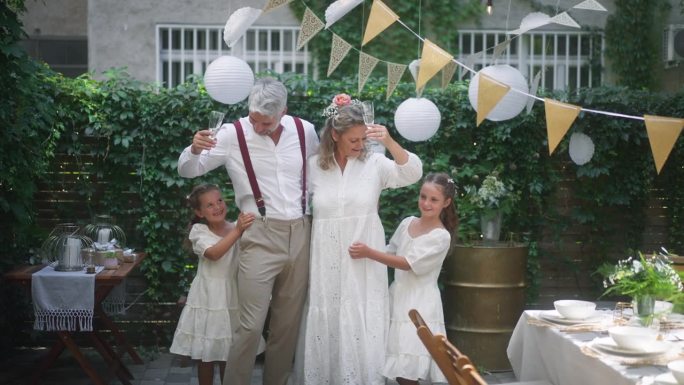 成熟的新娘和新郎与他们的女儿在后院的婚礼招待会上敬酒。