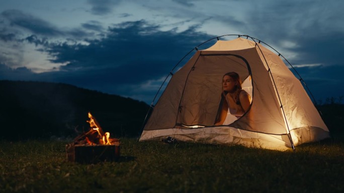 年轻女子拉开帐篷的拉链，在篝火旁眺望