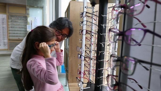 快乐的拉丁美洲女孩和她的祖父在验光店买眼镜