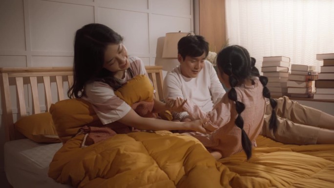 幸福的韩国家庭在早上:活跃和顽皮的孩子跑到她的父母的卧室叫醒他们。兴奋的小女孩强迫她的父母下床一起度