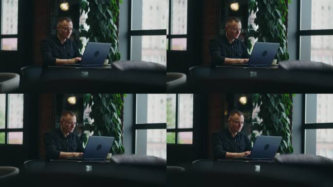 戴眼镜的帅哥在咖啡馆用笔记本电脑工作，自由职业者或网页开发人员的肖像