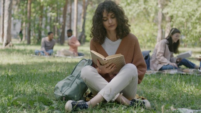 美丽的年轻女学生在公园里读书准备考试的肖像