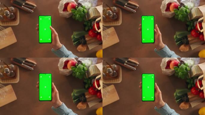 顶部静态视图匿名妇女使用智能手机与模拟绿色屏幕Chromakey显示在厨房餐桌上的食物配料。女性查看