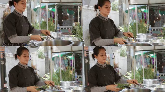 亚洲女厨师正在烹饪著名的泰国街头小吃“泰式炒面”，她一边炒面一边翻炒面条。