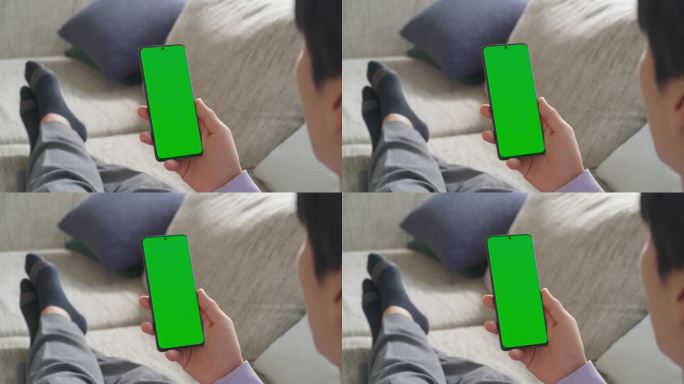 一个匿名男性在家里放松的镜头，使用带有绿色屏幕模拟显示的智能手机，从远程工作地点无缝管理任务和项目