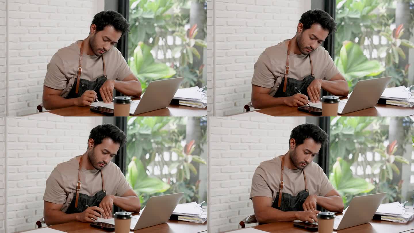 英俊的印度男人是一名咖啡师，也是一家小咖啡馆的老板。坐在桌边，认真地准备用笔记本电脑在网上订购咖啡店