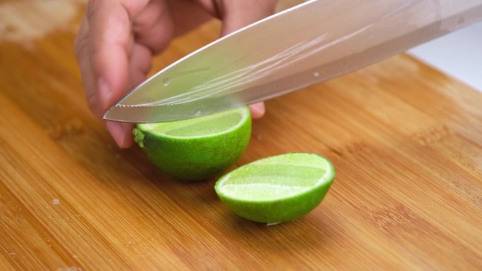 厨房里，女手持刀在木板上切青柠。把新鲜柠檬切成两半。高维生素C天然