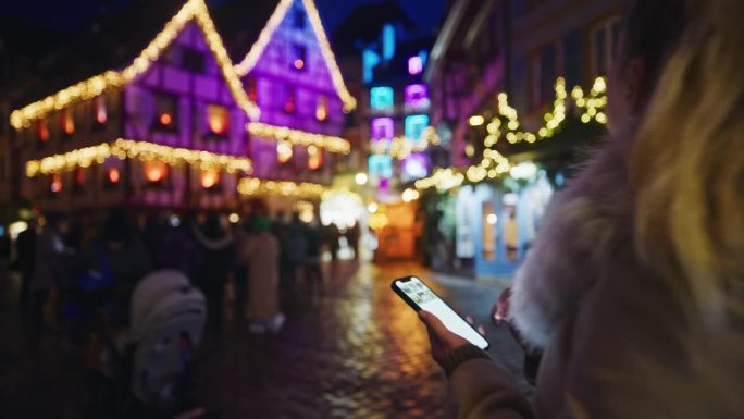 一名女子在科尔马一个热闹的圣诞市场漫步时使用着她的智能手机