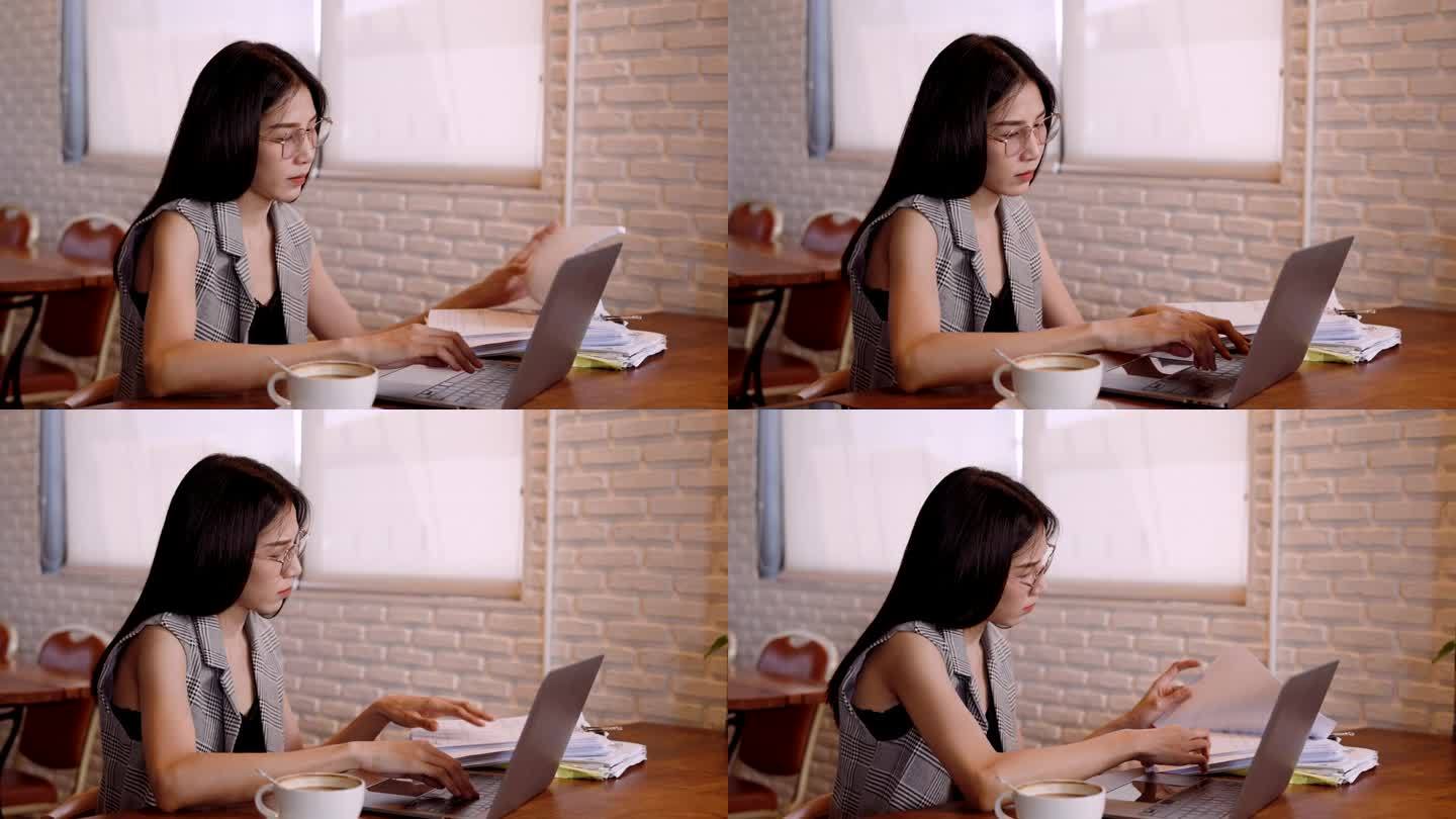 咖啡店老板，我是有意为之的。漂亮的亚洲女人坐在桌子上使用笔记本电脑。检查文档的正确性。