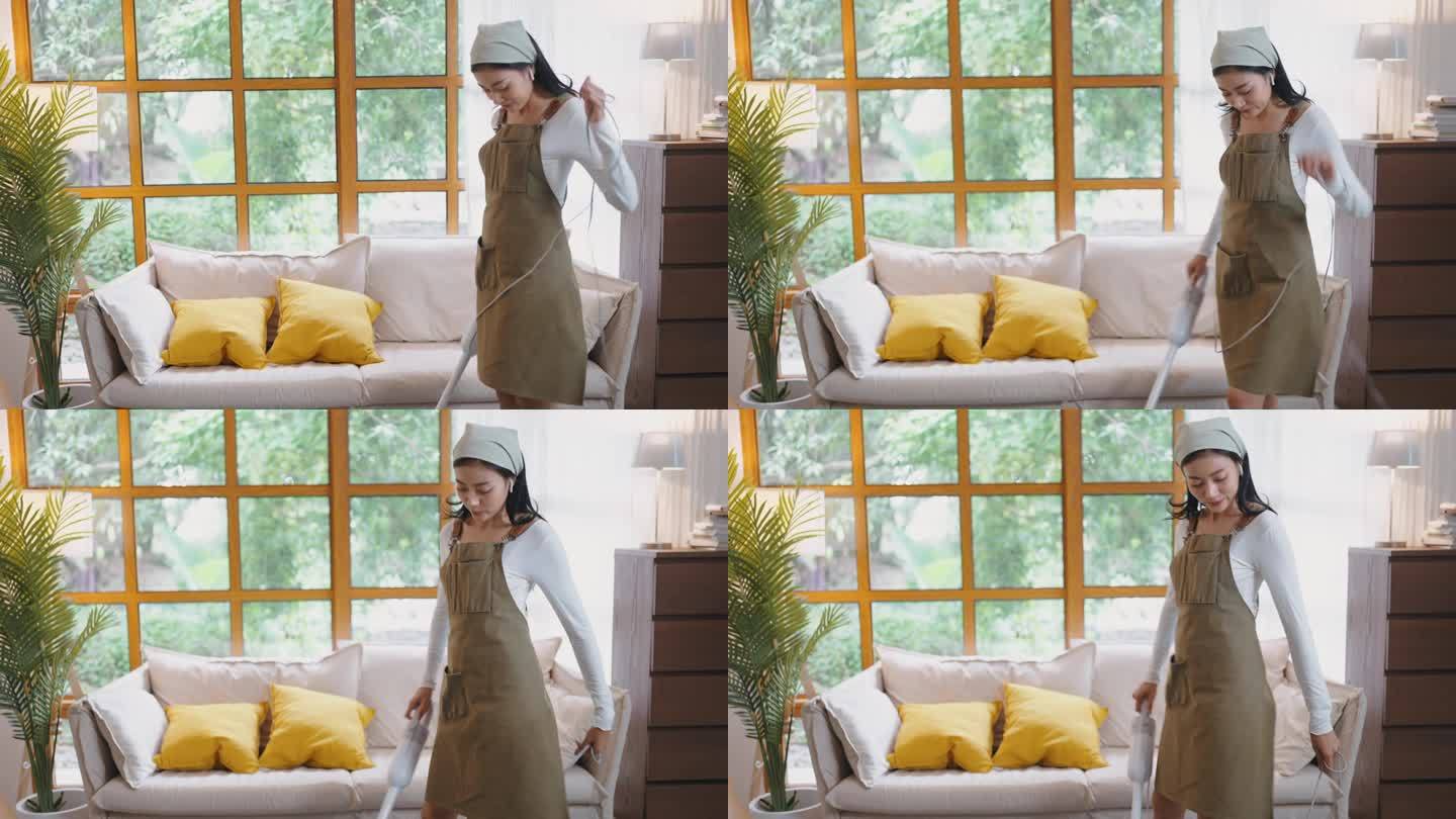 亚洲女性做家务在家里吸尘，在家里打扫房间时戴着耳机跳舞唱歌听音乐