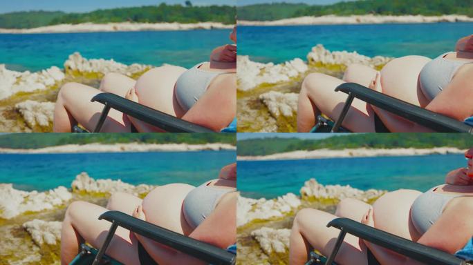 一位孕妇在海上享受产假。孕妇在沙滩上的躺椅上抚摸腹部