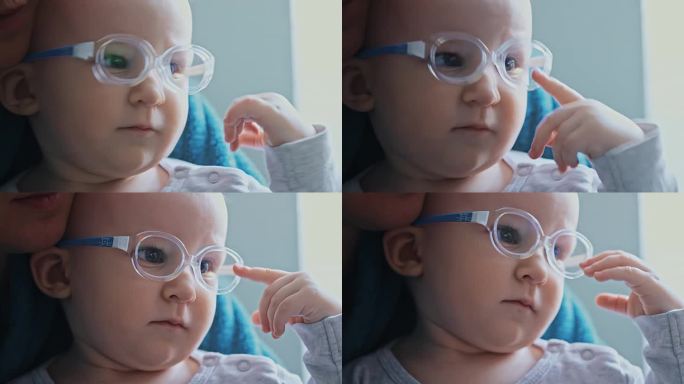 一个一岁的小女孩在看电视的时候用手指碰坏了眼镜。白种人婴儿有斜视、眼疾。视力不佳。孩子坐在妈妈的腿上