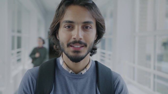 慢镜头拍摄的是一个兴高采烈的阿拉伯青年背着双肩包站在大学大厅里，学生们四处走动