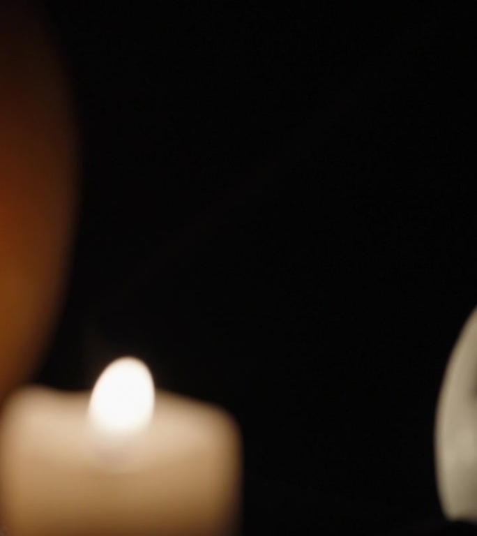 垂直视频。两个万圣节南瓜，一个是白色的，上面插着蜡烛。照相机慢慢聚焦在他们身上。