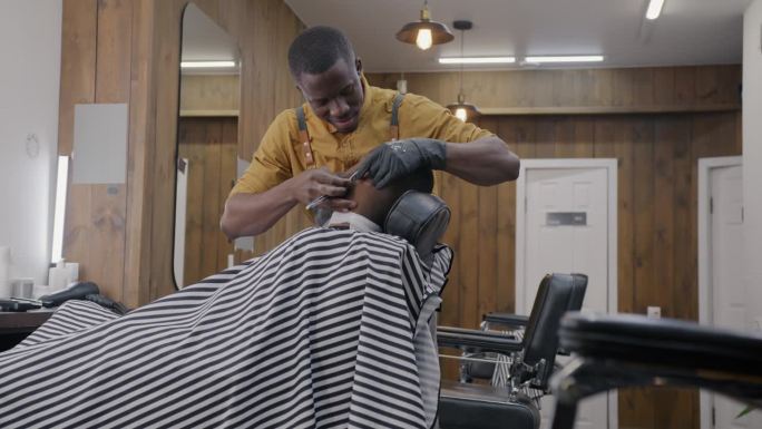 专业理发师在理发店里给非裔美国人刮胡子，微笑着与顾客交谈