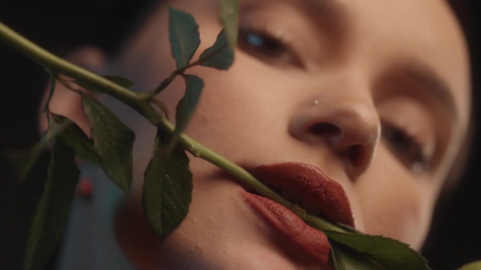 性感的女人用红色的口红黑色的背景工作室拍摄摆姿势与一个白玫瑰在她的牙齿