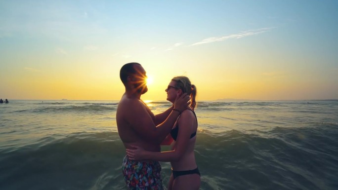 夏天旅行、度假时，一对相爱的情侣在海滩上一起看日落。拥抱的夫妇的剪影享受日落，日出的海洋在热带目的地