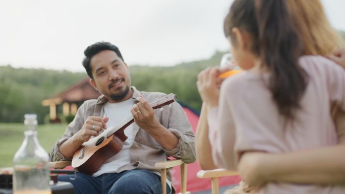 快乐的父亲在露营地给他的家人弹奏四弦琴。