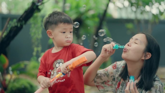 无忧无虑的夏日乐趣:亚洲男孩和他的妈妈在公园吹泡泡-户外快乐和亲密