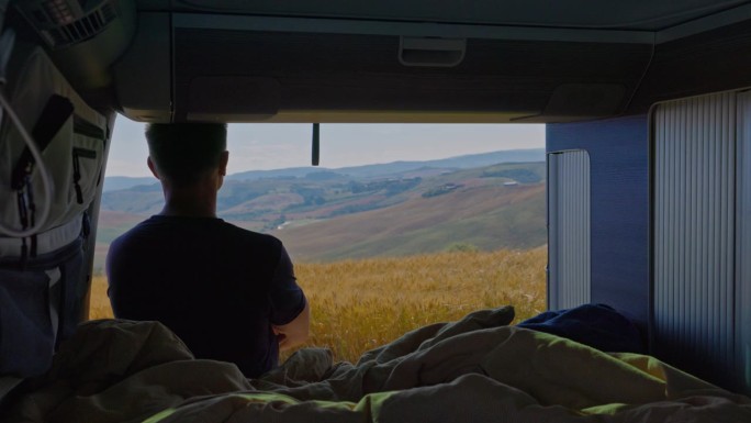 一名男子站在露营车外，眺望托斯卡纳田园诗般的乡村景色