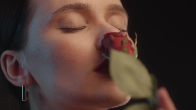 性感的女人用红色的口红黑色的背景工作室拍摄的姿势闻着一朵红玫瑰和调情的镜头