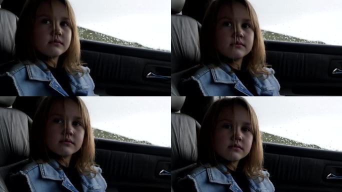 一个可爱的欧洲七岁女孩穿着牛仔背心坐在车里看着。下雨天，一个小女孩坐在一辆有真皮座椅的汽车里的副驾驶