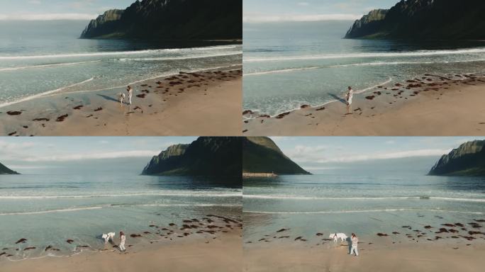 美丽的全景，十几岁的女孩在厄斯峡湾海滩上与大白色狗玩耍