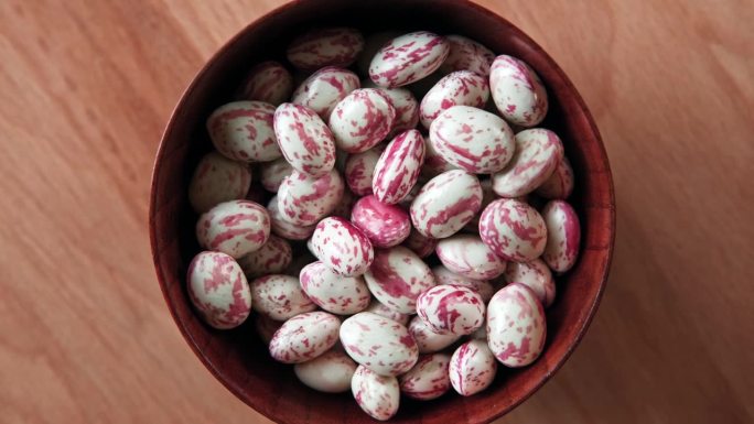 蔓越莓豆在旋转。木碗里的Borlotti豆荚。前视图。时尚的现代美食背景。红色的颜色。创意食品平铺。