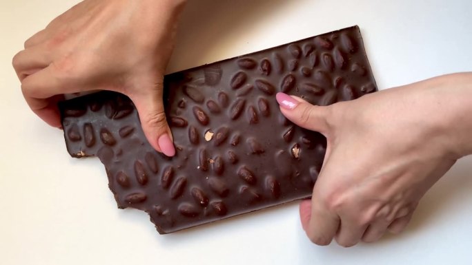 一名女子双手掰碎白色背景的黑巧克力棒。俯视图坚果零食视频。高品质4k画面