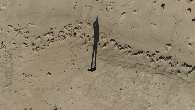 俯视图，年轻女子独自走在沙滩上长长的影子。