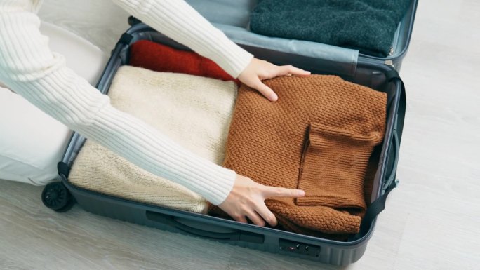 一名妇女用手把冬衣装进行李箱。时间旅行，旅行，放松，春秋季或冬季的季节和度假的概念
