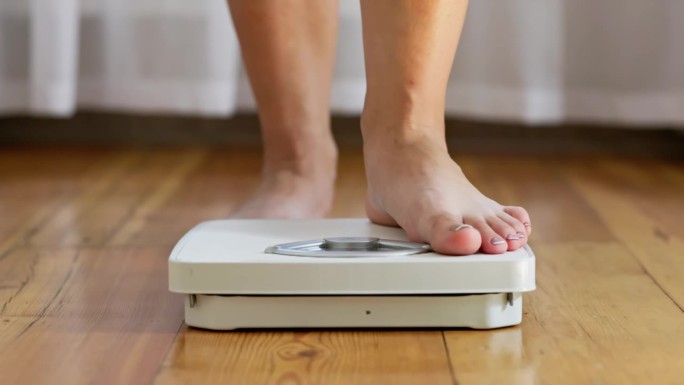 一位女士站在地板上的白色磅秤上量体重