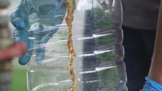 一名戴蓝色橡胶手套的男子打开水龙头，将精制的生物柴油注入一个透明的塑料水箱。
