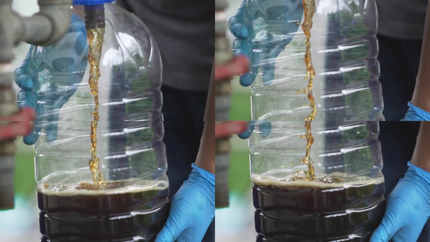 一名戴蓝色橡胶手套的男子打开水龙头，将精制的生物柴油注入一个透明的塑料水箱。