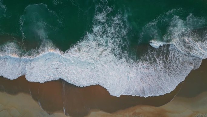 日落时分，沙滩上的浪花泛起白色泡沫。空中俯瞰海景或海洋沙滩