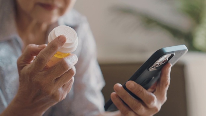 老妇人拿着药瓶，自己用智能手机应用程序在网上填药。