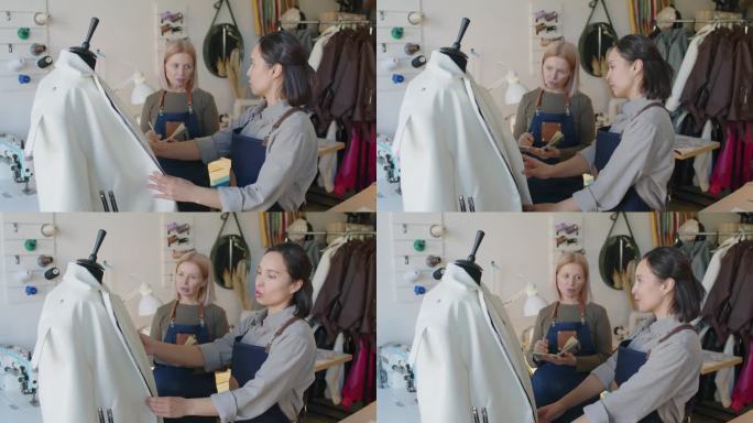 两个女裁缝给假人穿上皮夹克，在工作室聊天
