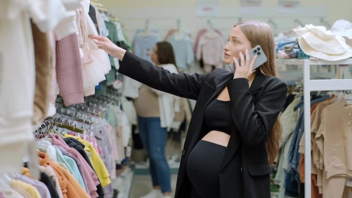 孕妇拿着手机在童装店选购婴儿服装